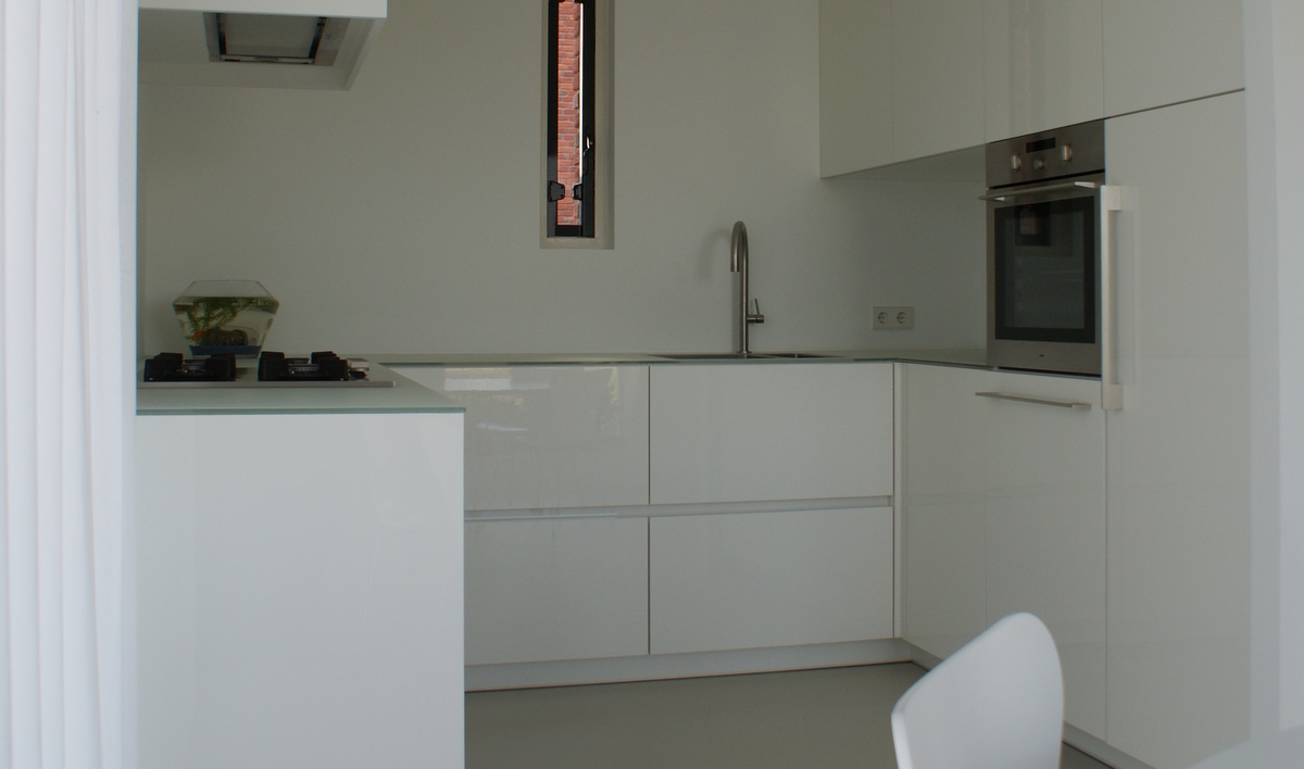 Strakke witte hoogglans u-keuken met glazen werkblad en Atag apparatuur